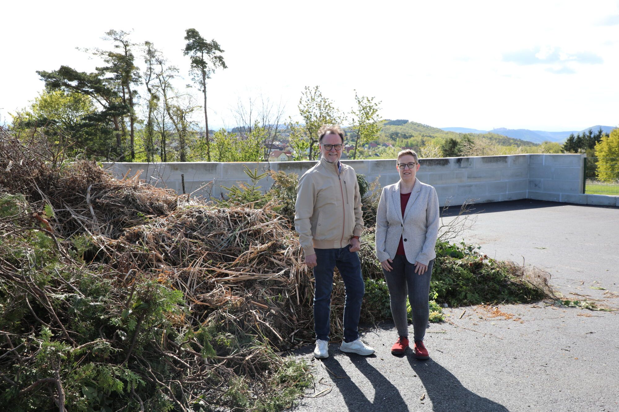 Stadtrat Werner St&ouml;berl und Abfallwirtschaftsamtsleiterin Martina G&auml;rtner stehen vor dem neuen Strauchschnittsammelplatz, wo schon Strauchschnitt im Hintergrund abgelagert wurde.