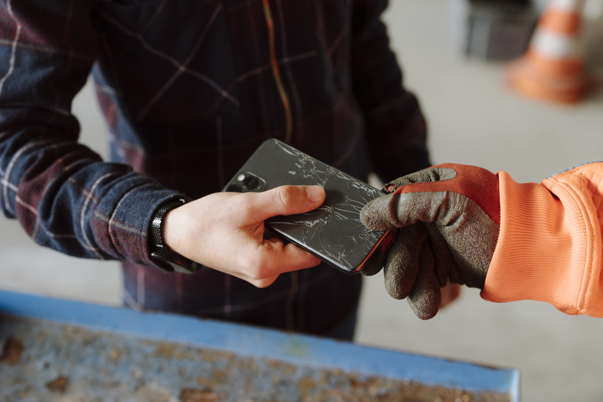 Man sieht den Ausschnitt einer Männerhand, die ein defektes Handy einem WSZ-Mitarbeiterhand übergibt. 