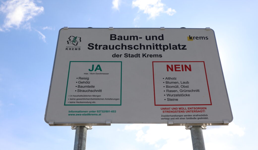 Das Foto zeigt eine weiße Tafel für den Strauchschnittsammelplatz mit der Erklärung, wie richtig entsorgt wird.